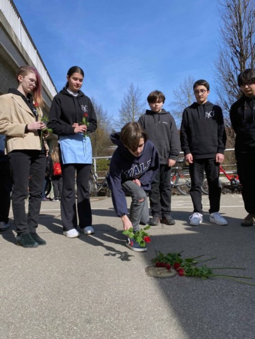 Schülerinnen und Schüler legen Rosen nieder.